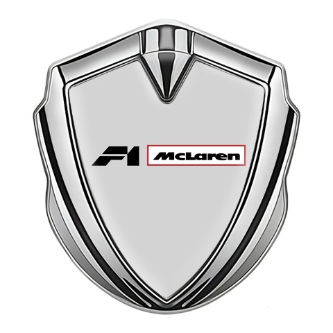 Mclaren Emblem Abzeichen selbstklebend Silbertonfarbe Grau Hintergrund mit F1 Logo