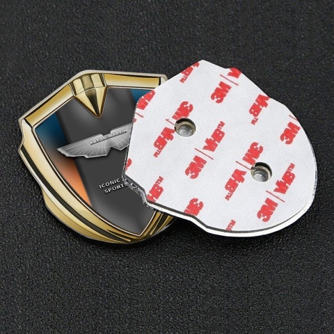 Aston Martin Emblem Abzeichen Goldtonfarbe mit Orange Blau Hintergrund und Grau logo